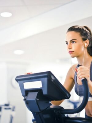 Serious fit woman in earphones and activewear listening to music and running on treadmill in light contemporary sports center